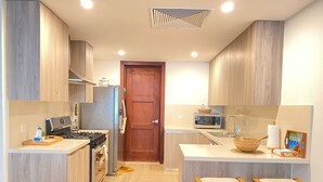 A compact kitchen with wooden cabinets, a microwave, a stove, and two bar stools. - 2BR 6 Guest Balcony in Portillo Close to Beach (Las Terrenas)