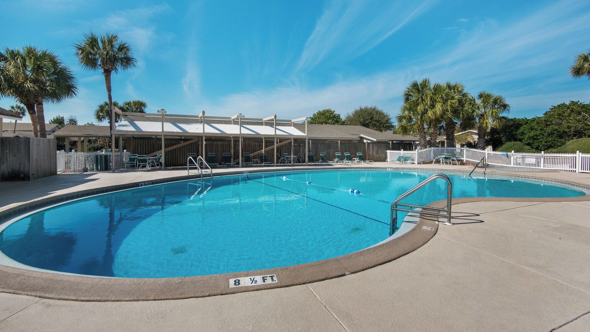 A swimming pool with a lifeguard chair, a covered seating area, and a fenced deck.