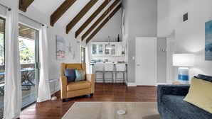 Un salón espacioso con un sillón de cuero, un sofá azul y una cocina al fondo.