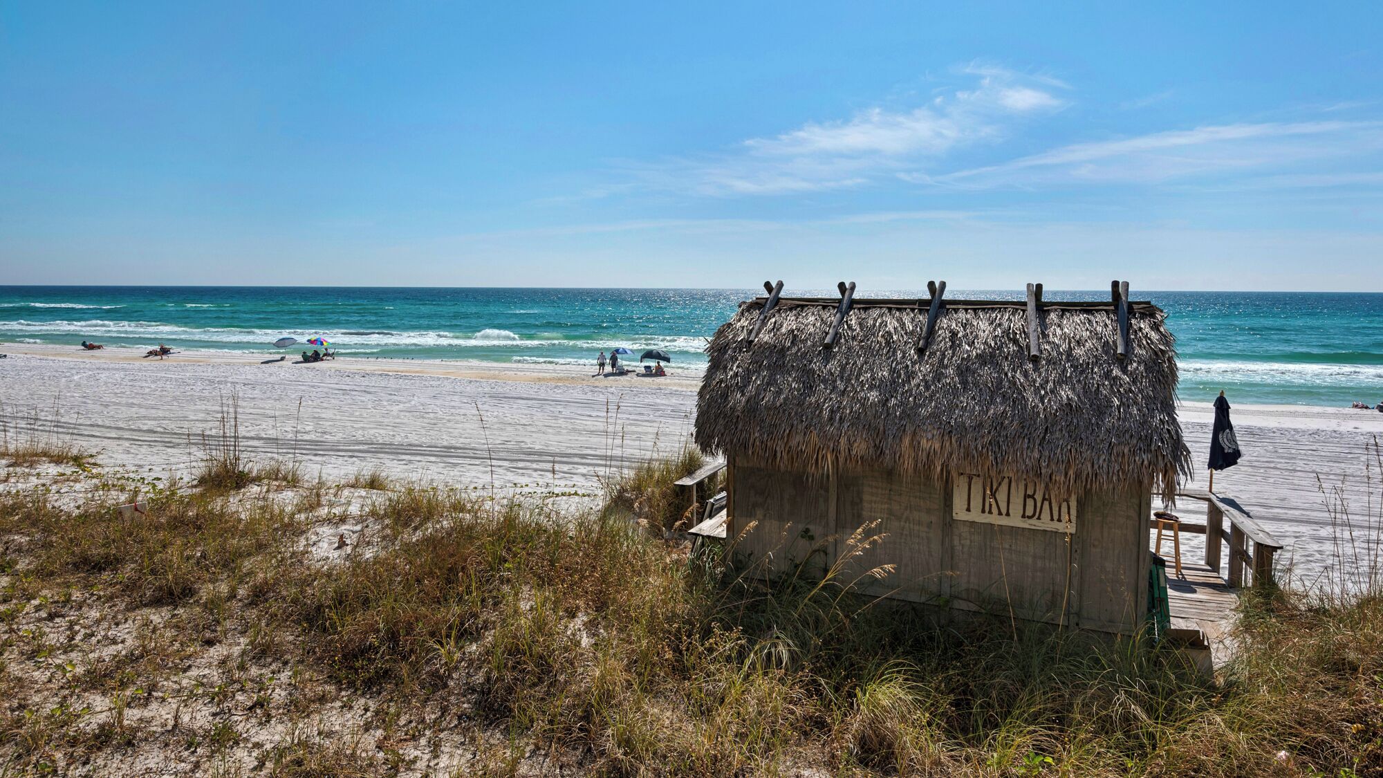 A beach hut labeled "TKIBAN" with a thatched roof, situated on a sandy beach with the ocean in the background.