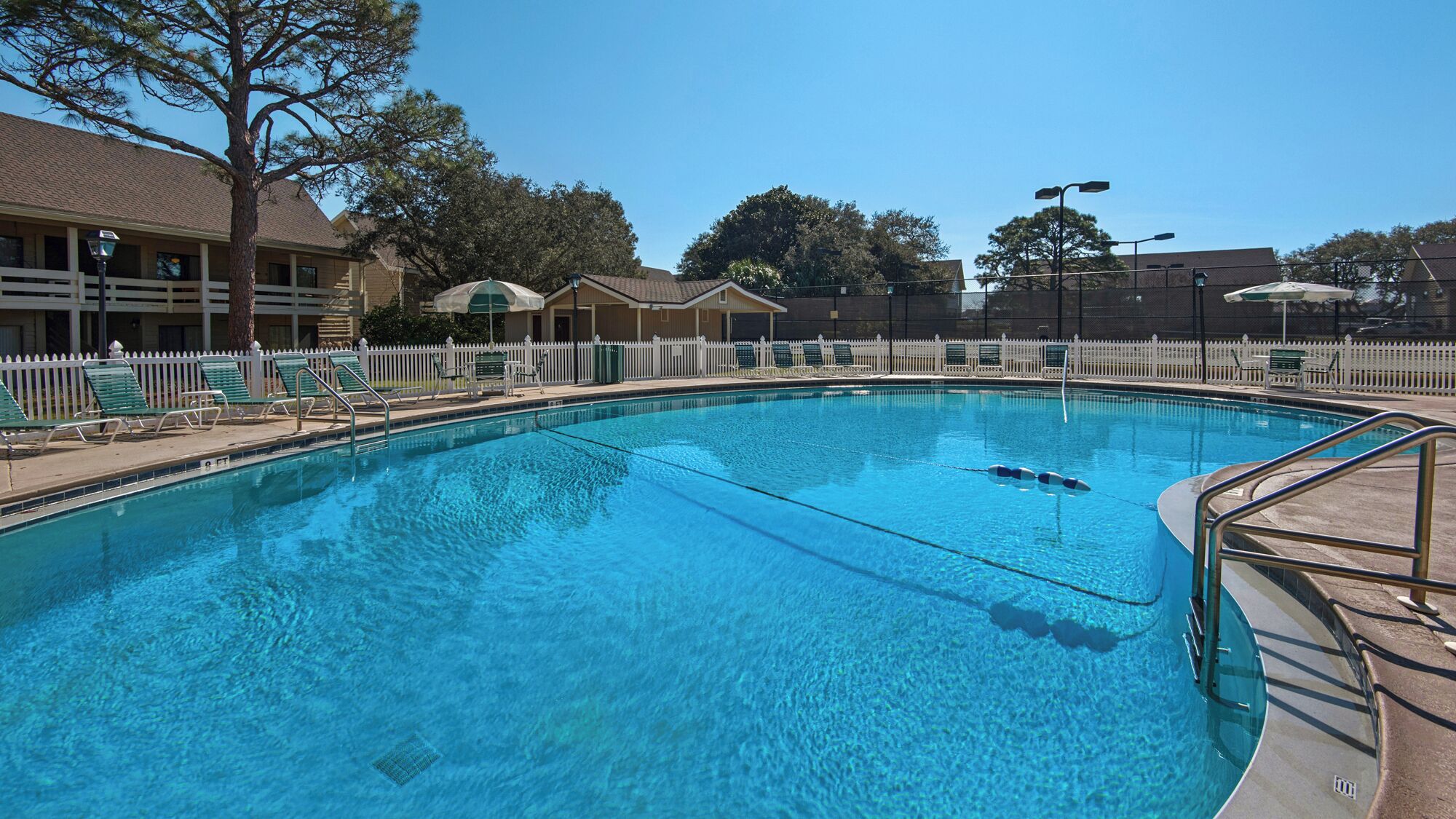 A swimming pool with lounge chairs and a white fence.