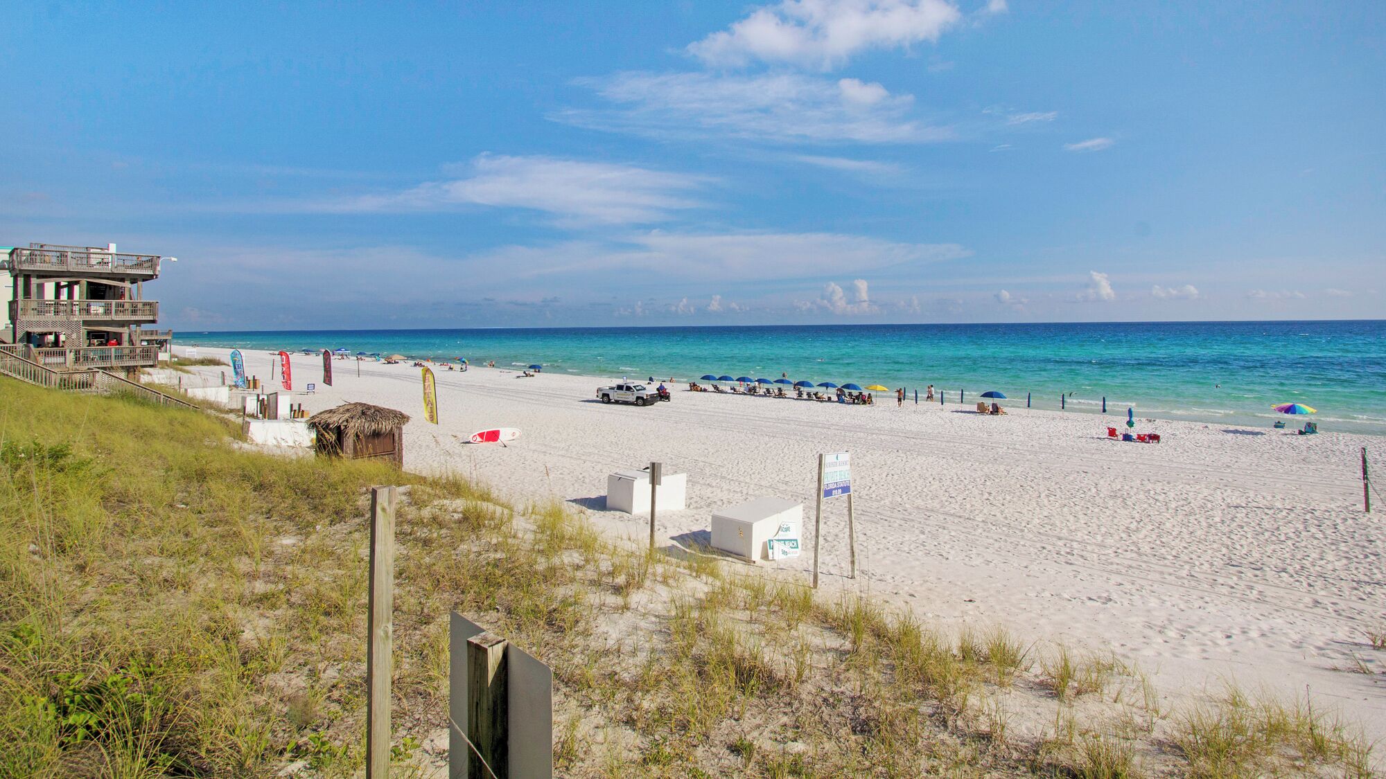A beach with a building, umbrellas, and beach chairs.