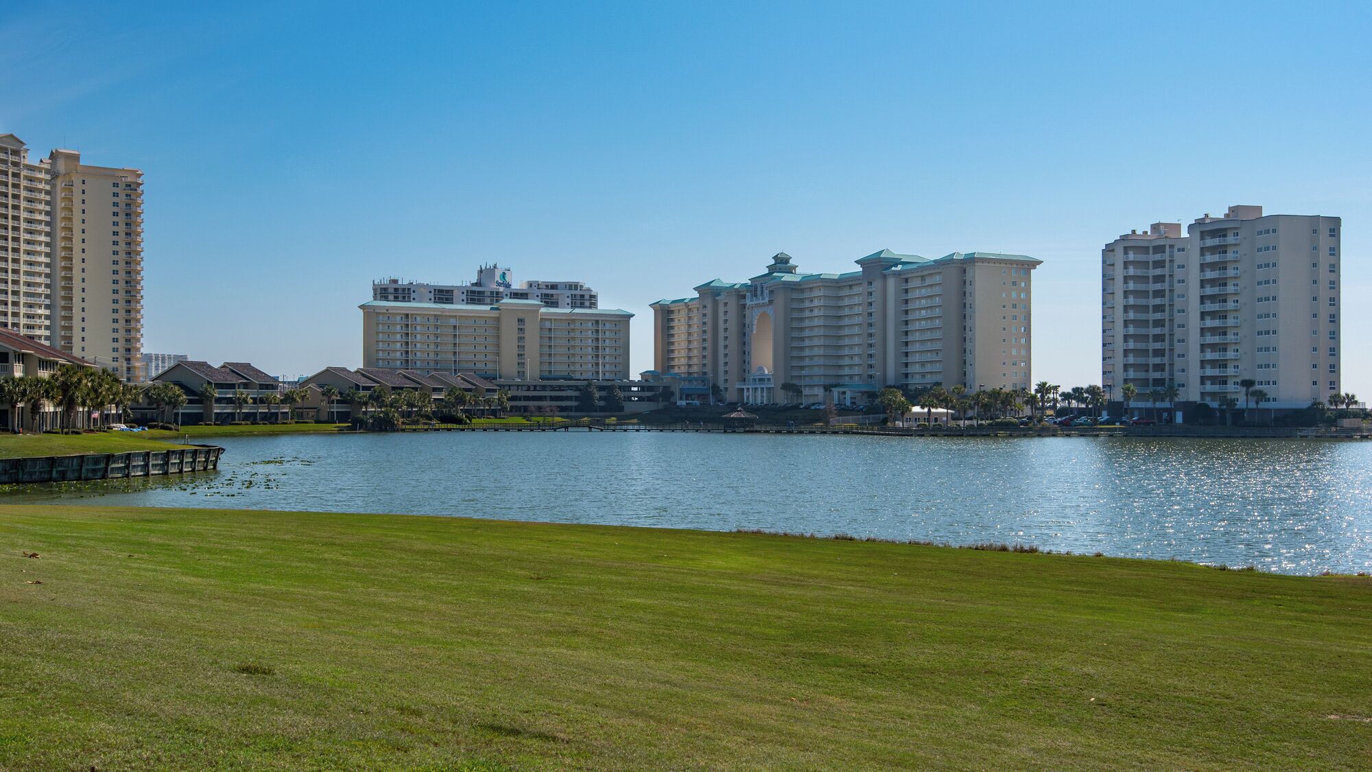 A waterfront hotel with multiple high-rise buildings, a grassy area in the foreground, and a body of water.