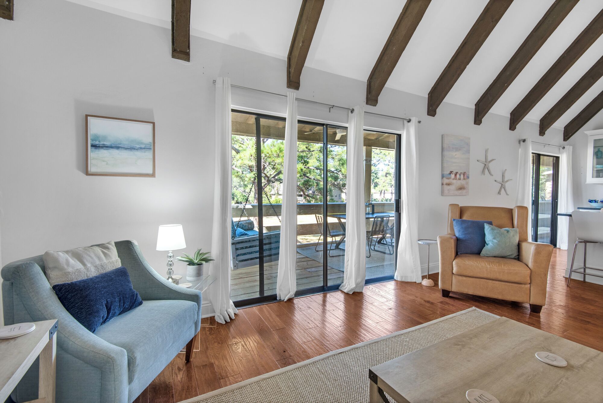 A living room with a sofa, a chair, a coffee table, and a view through glass doors to an outdoor area with a swing.