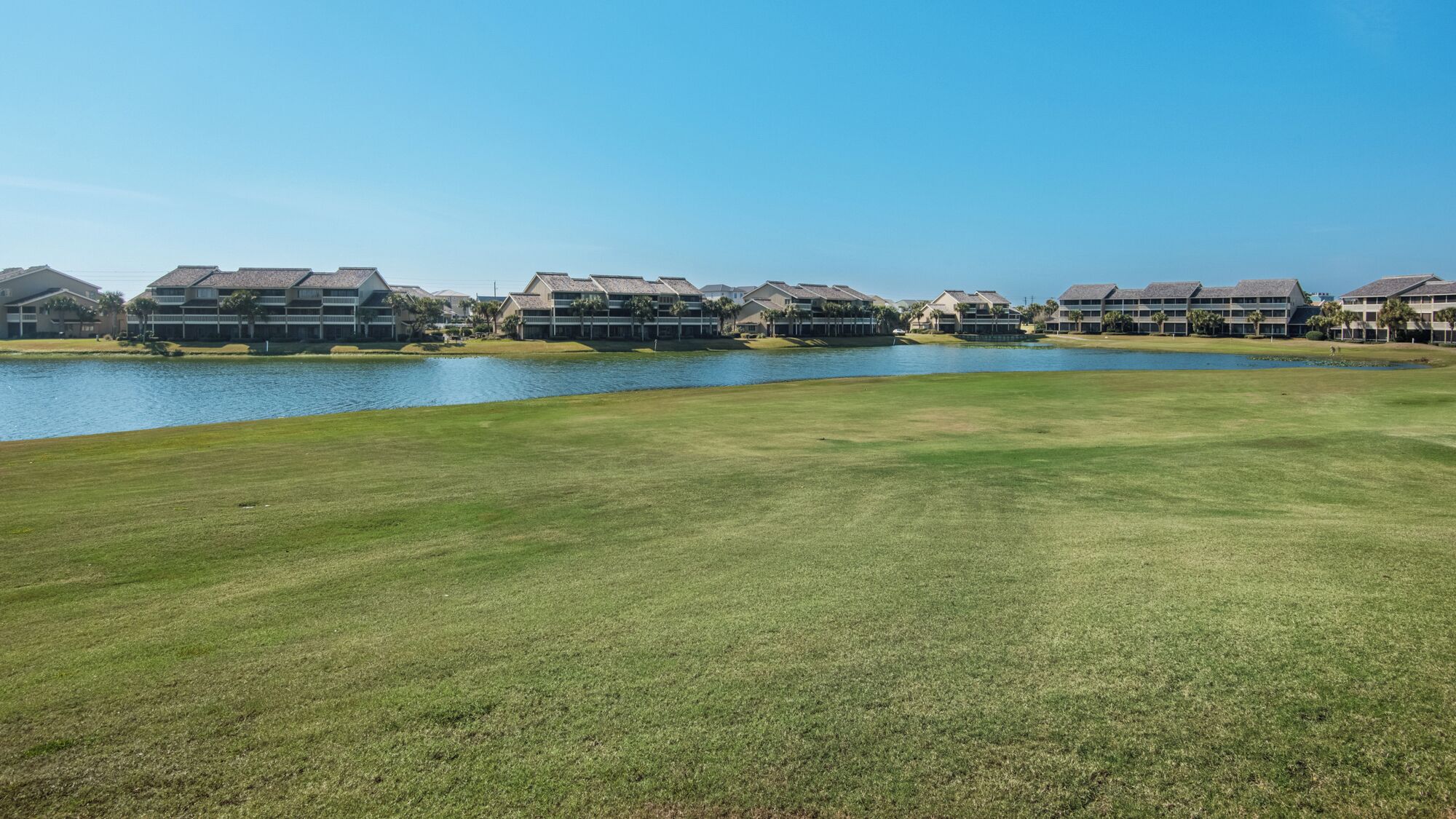 A golf course with a water body and multiple buildings in the background.