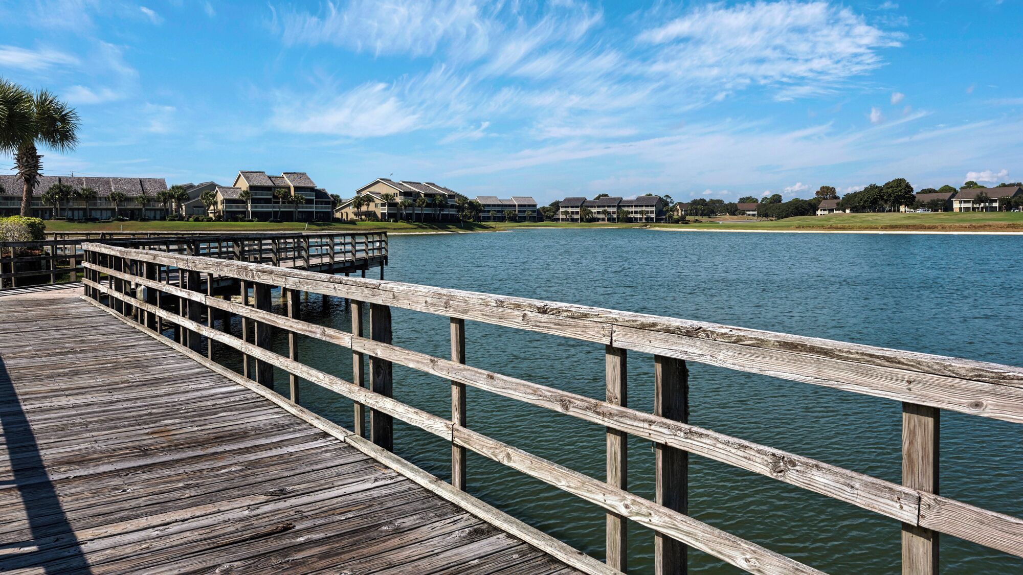 A wooden pier extending over calm water, leading to a row of houses with sloped roofs.