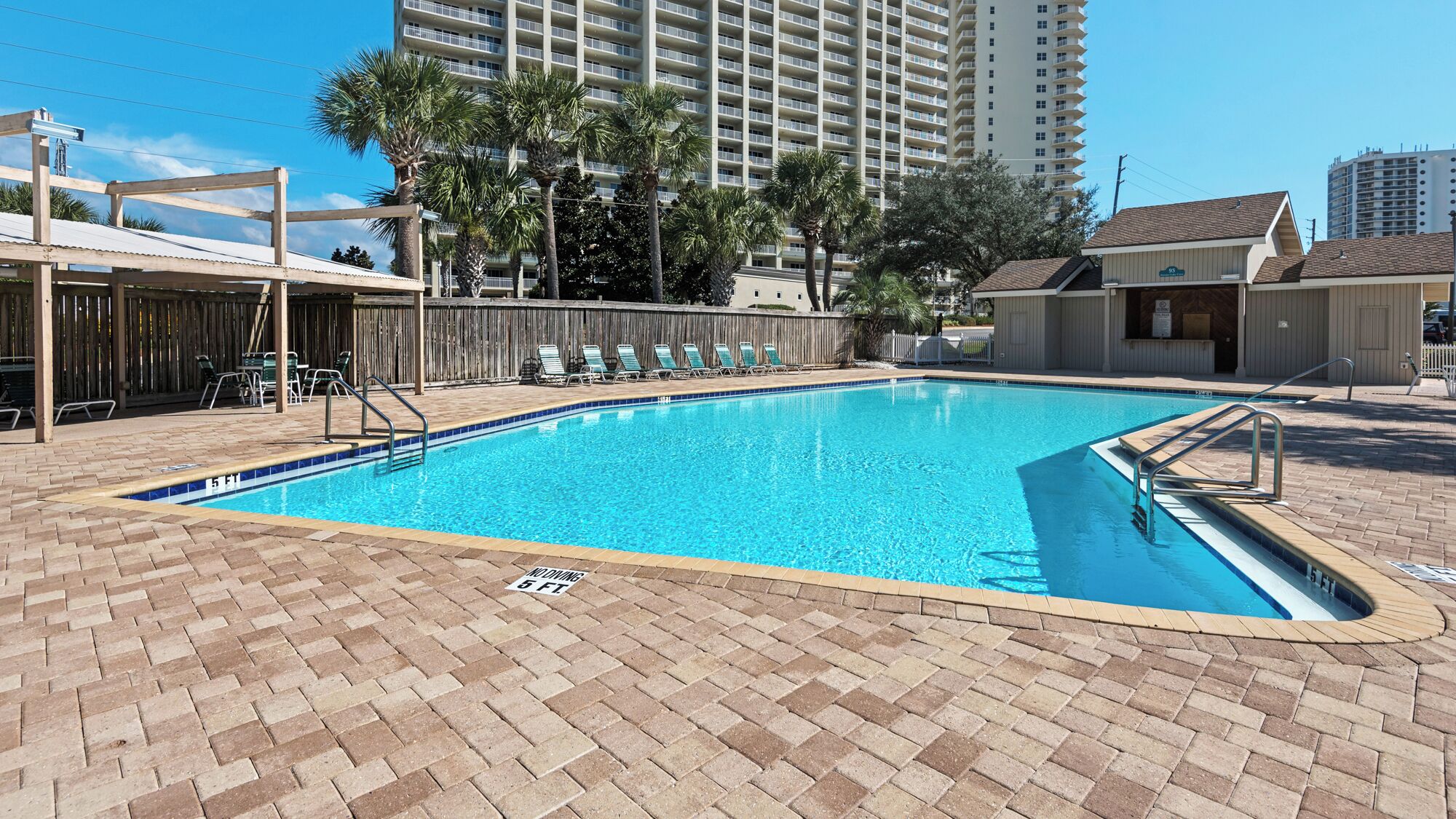 A swimming pool with a brick deck, surrounded by lounge chairs and a wooden fence.