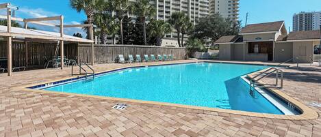 A swimming pool with a brick deck, surrounded by lounge chairs and a wooden fence.