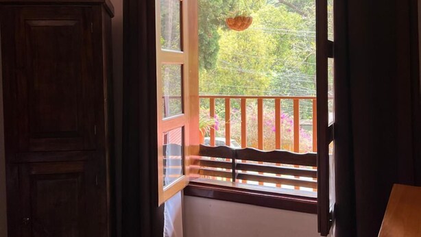 Una habitación con un armario de madera, una ventana con vistas a la vegetación exterior y un balcón con barandilla.