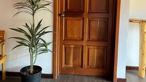 Una puerta de madera con el número 5 encima, una planta en maceta a un lado y un banco de madera a la izquierda.