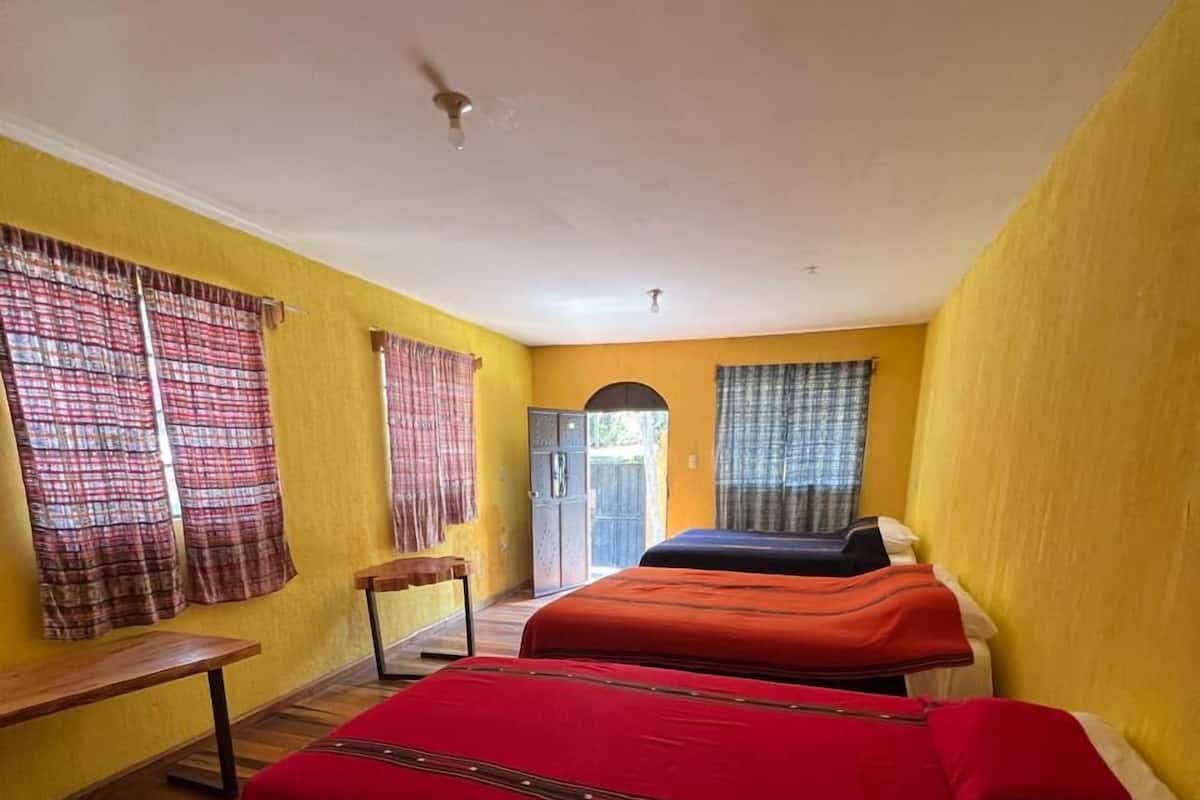 Una habitación con dos camas, suelo de madera, paredes amarillas y un banco.