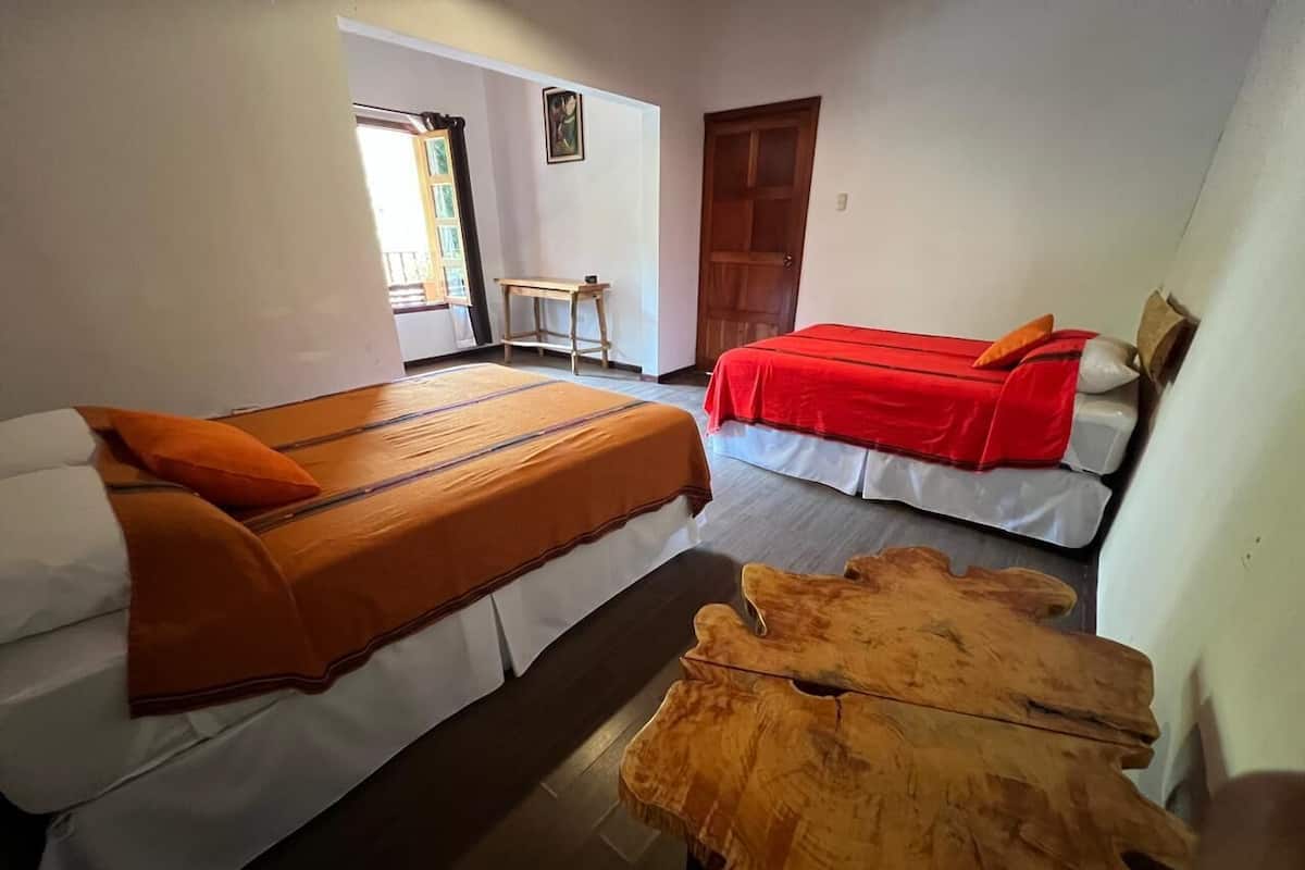 Una habitación con dos camas, cada una con colcha roja y blanca, y una mesa de centro de madera en el centro.