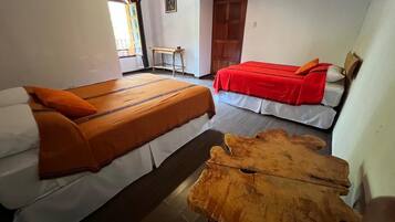 Una habitación con dos camas, cada una con colcha roja y blanca, y una mesa de centro de madera en el centro.