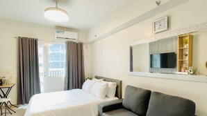 A hotel room with a bed, a dark sofa, a TV, and a window with curtains. - Experience the Perfect Studio Retreat in Iloilo City (Iloilo City)