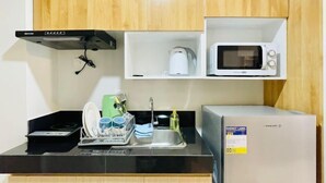 A compact kitchen with wooden cabinets, a microwave, a kettle, a sink, and a refrigerator. - Experience the Perfect Studio Retreat in Iloilo City (Iloilo City)