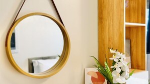 A round mirror hanging on a wall, a wooden shelf with a vase of white flowers, and a small white sculpture on a wooden table. - Experience the Perfect Studio Retreat in Iloilo City (Iloilo City)