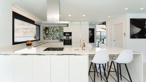 A modern kitchen with white cabinetry, a central island with bar stools, and a large window providing natural light.