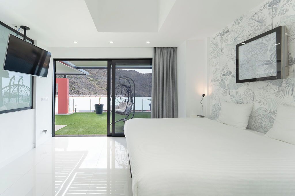 Een moderne slaapkamer met een groot bed, een televisie en een schuifdeur naar een balkon met uitzicht op de bergen.