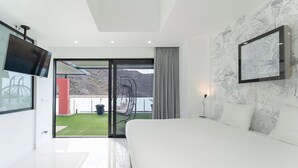 A modern bedroom with a large bed, a television, and a sliding glass door leading to a balcony with a view of the mountains.