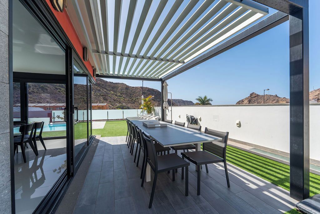 Un patio al aire libre con mesa, sillas y una pérgola.