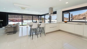 A modern kitchen with a dining area, large windows, and a view of the landscape.
