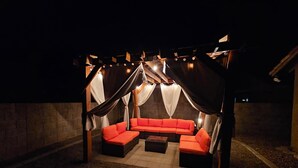 An outdoor seating area with a red sofa and cushions, under a canopy with draped fabric. - Rita Ranch Retreat - Cozy 4 BD (Tucson)