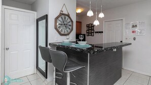 A kitchen with a central island, two bar stools, pendant lights, a wall clock, and framed pictures. - 1bd 1bth , PYT , Airport , MPT (Fort Lauderdale)