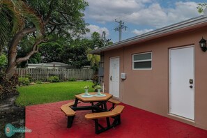 A small house with a red patio, a picnic table, and a white door.