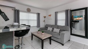 Ein modernes Wohnzimmer mit grauem Sofa, Couchtisch, Essbereich mit Barhocker und Wand-Fernseher.