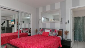 Ein Hotelzimmer mit zwei Betten, einem großen Spiegel, einem Fernseher und einem Badezimmer mit Duschvorhang.