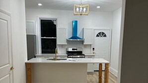 A modern kitchen with a central island, white cabinetry, and a blue range hood. - Diamond in the Burgh (Pittsburgh)