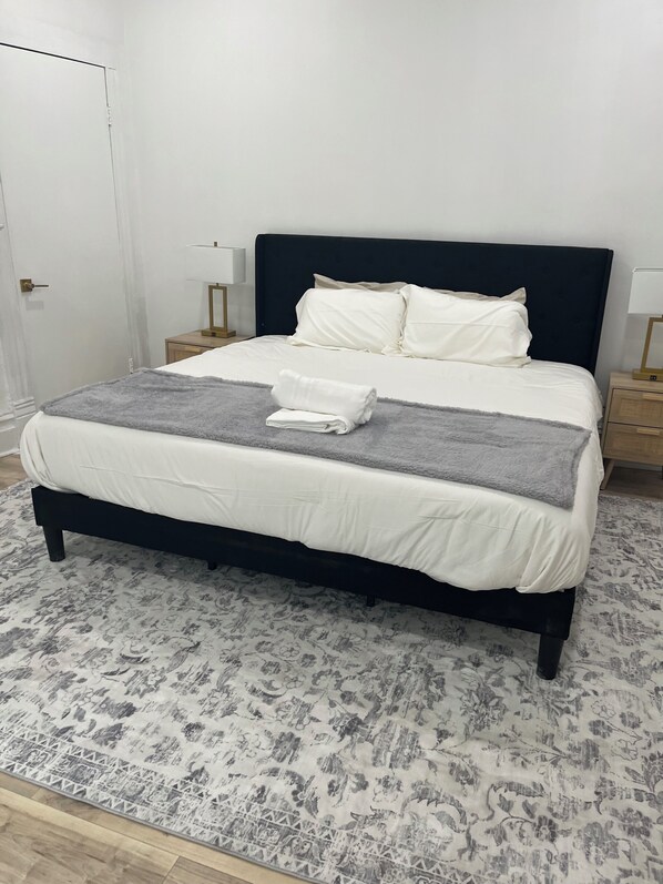 A neatly made bed with white linens and a grey blanket, a dark headboard, and two bedside tables with lamps.