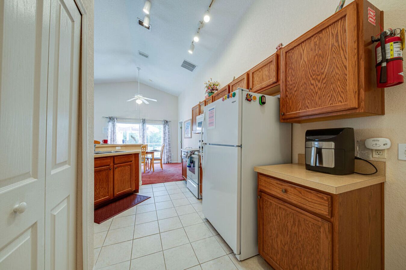 A compact kitchen with wooden cabinets, a refrigerator, a coffee maker, and a fire extinguisher.