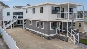 A two-story residential building with a balcony on the upper floor, a covered outdoor area, and a stone foundation.