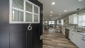 A modern kitchen with white cabinets, a black door with the number 6, and a wooden floor.