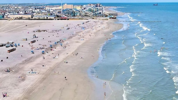 A beach with a roller coaster and buildings in the background.