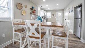 A modern kitchen with white cabinetry, a stainless steel refrigerator, and a dining area with white chairs and a wooden table.