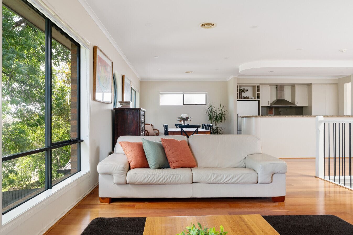 A spacious living room with a large window, a white sofa, and a kitchen in the background.