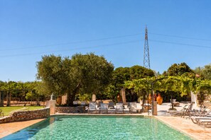Une piscine aux eaux cristallines, dotée de chaises longues et bordée d’un mur en pierre.