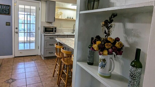 A kitchen with a microwave, wooden chairs, a white cabinet, and a shelf with decorative items. - Fort Huachuca. Home with private Gym. Pet with fee (Sierra Vista)