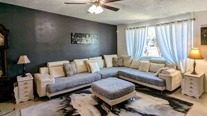 A living room with a sectional sofa, a ceiling fan, a window with curtains, a rug, and a lamp. - Fort Huachuca. Home with private Gym. Pet with fee (Sierra Vista)