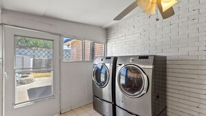 A laundry room with two stainless steel front-loading washers and dryers, a white brick wall, and a ceiling fan. - Central El Paso. 7 mins to Ft Bliss. (El Paso)