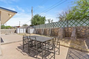 An outdoor patio with a metal table and chairs, surrounded by a stone wall and a green fence.