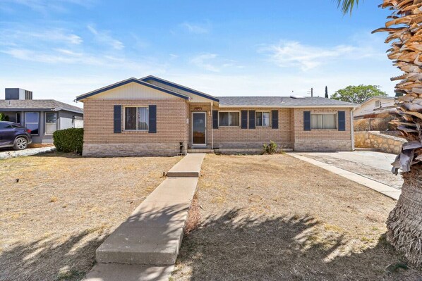 A two-story brick house with a front porch, a driveway, and a small yard.
