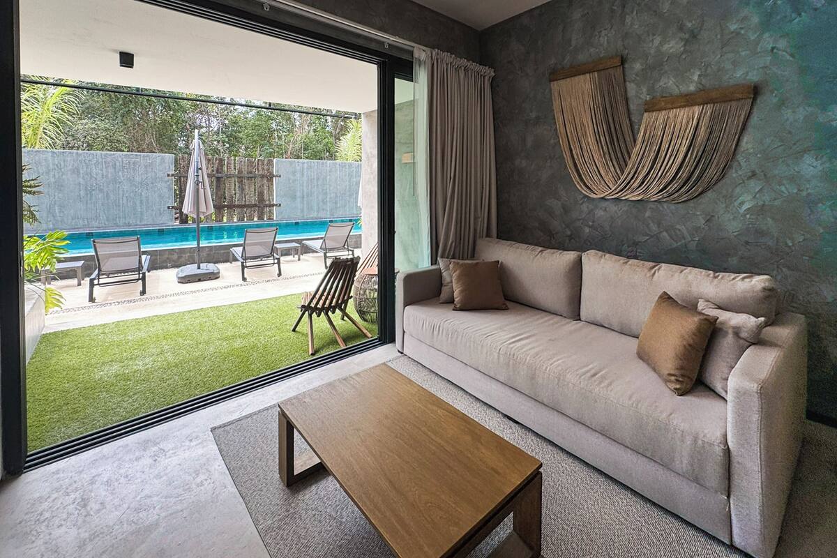 A modern living room with a sofa, a wooden coffee table, and a view of a swimming pool and garden.