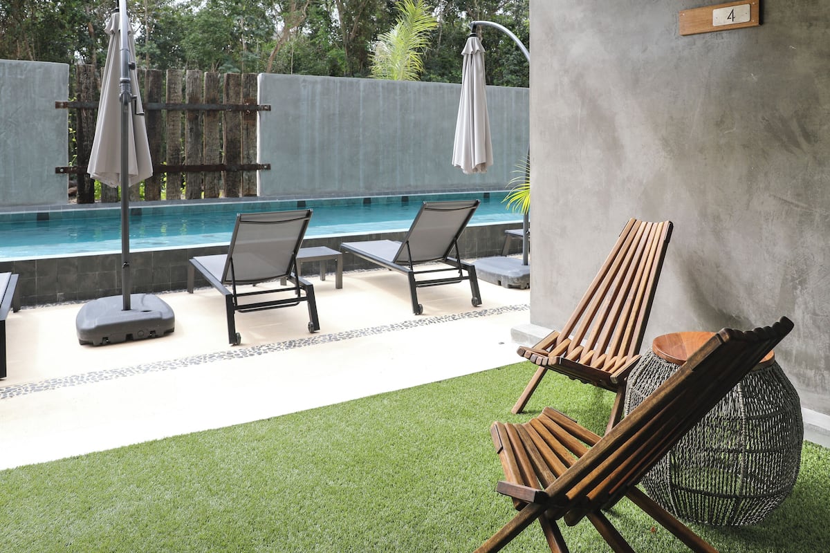 A pool area with two lounge chairs and a table, a wooden chair, and a woven basket.