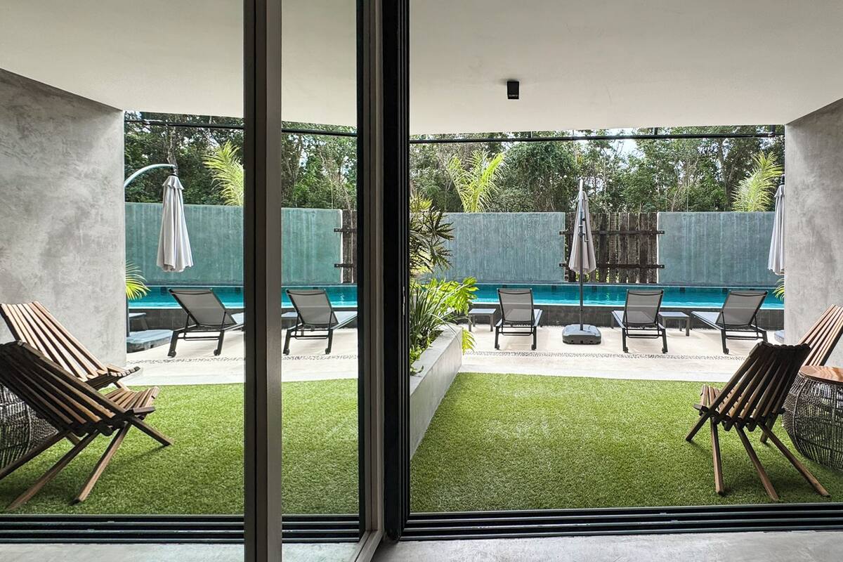 A modern indoor pool area with artificial grass, lounge chairs, and a view of the outside.