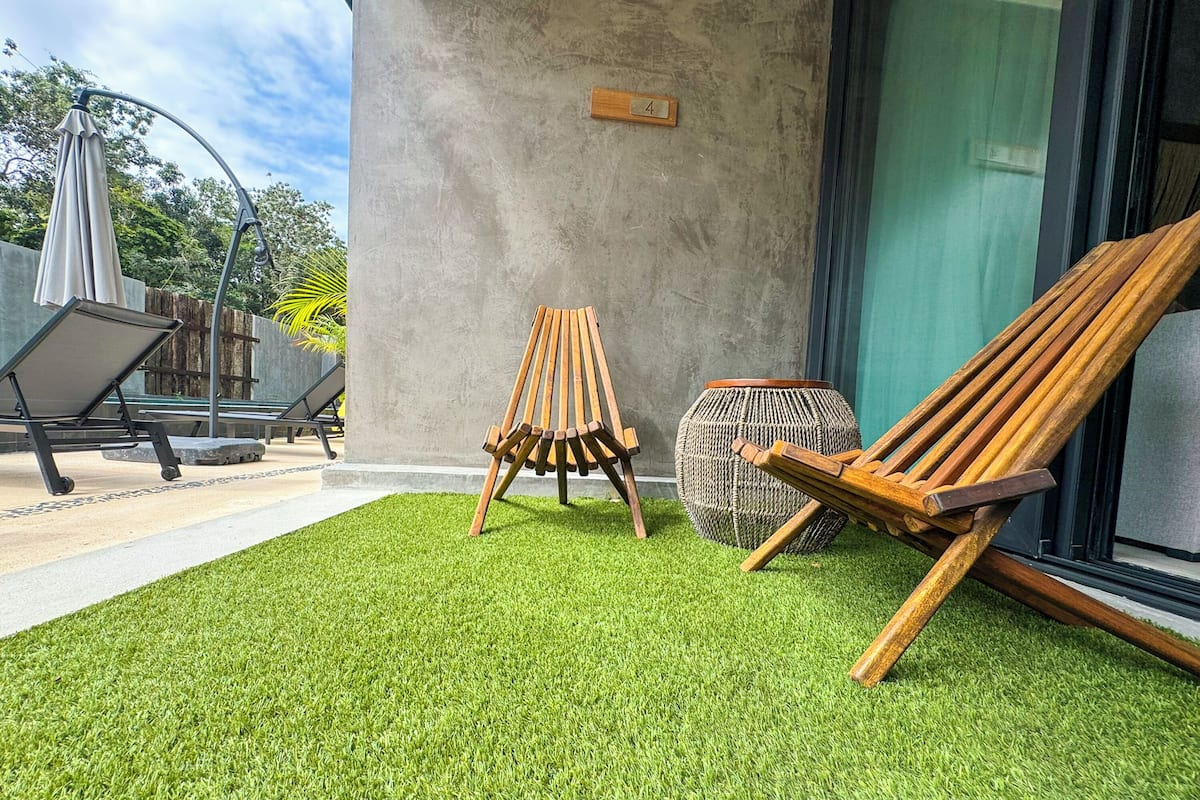 A patio with artificial grass, two wooden chairs, a woven basket, and a concrete wall with a wooden plaque.