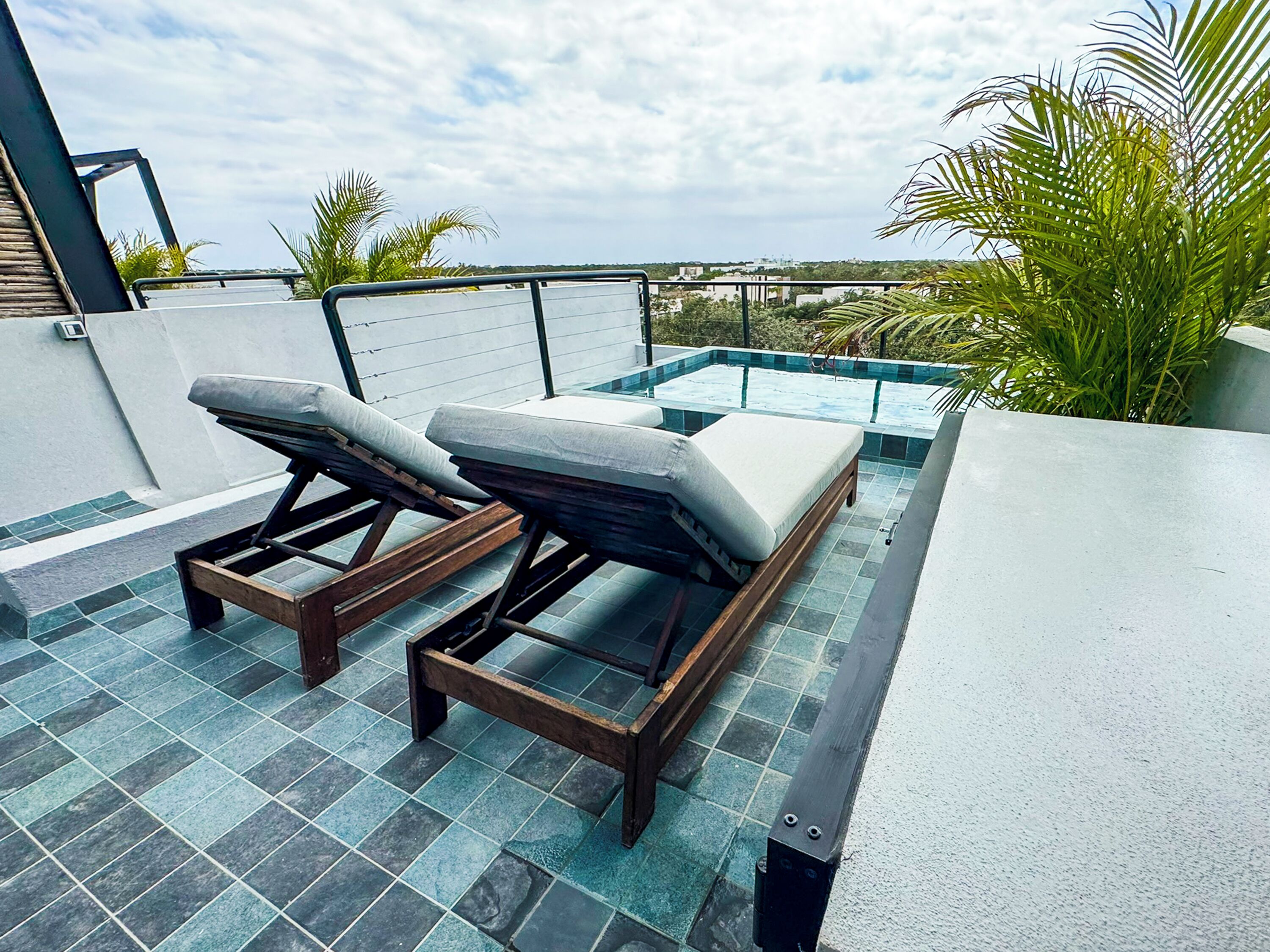 A rooftop terrace with two lounge chairs, a small pool, and a view of the cityscape.
