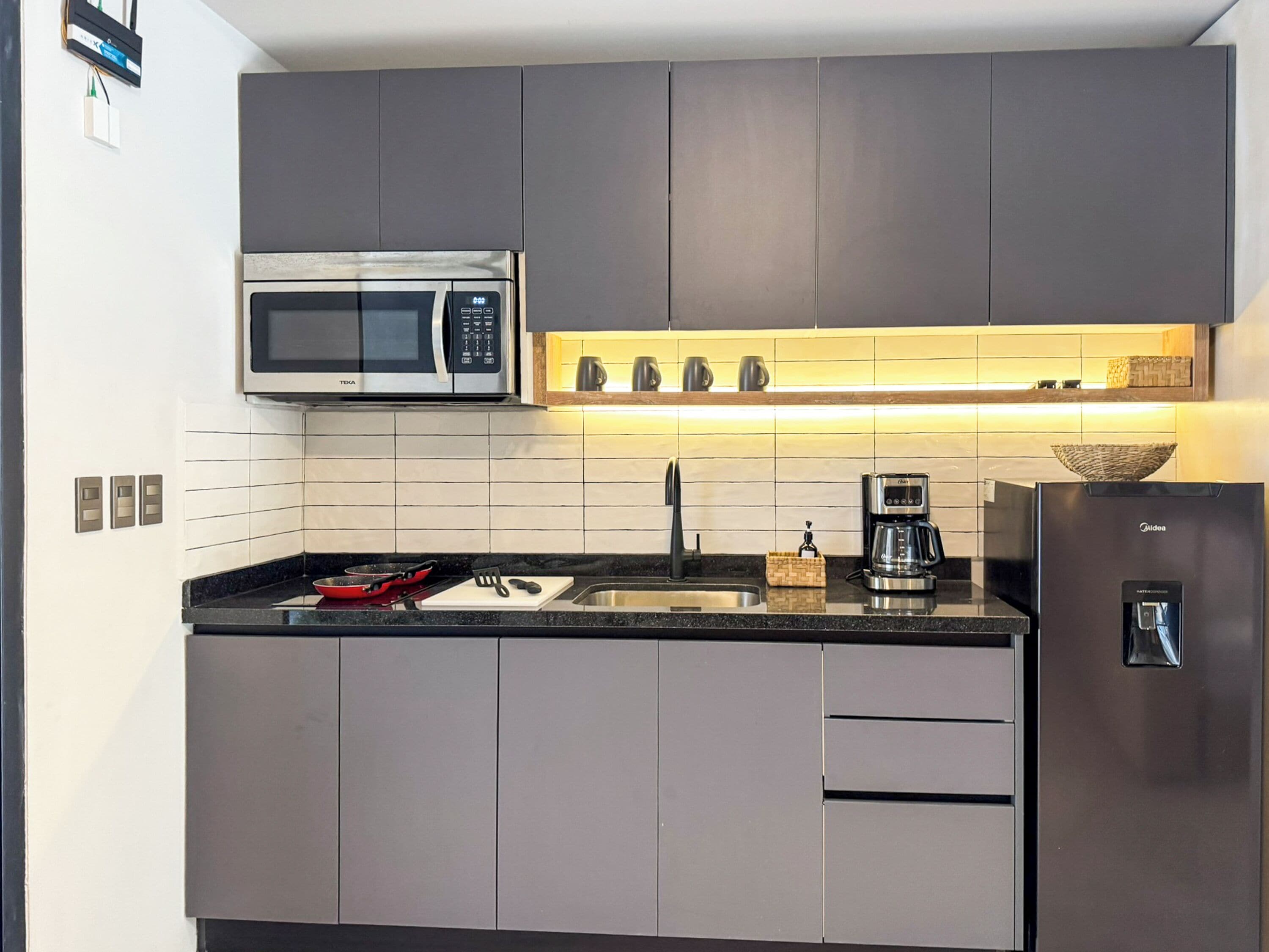 A modern kitchen with grey cabinets, a stainless steel microwave, a coffee maker, and a built-in oven.